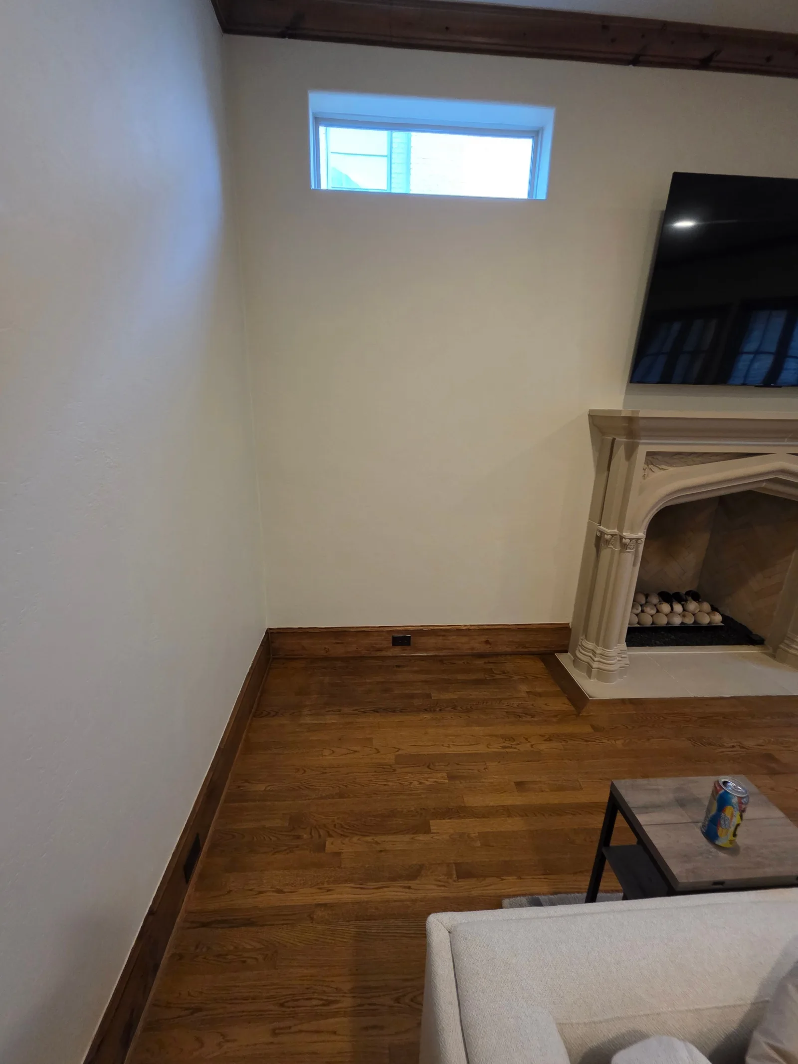 A living room wall with a restored cream finish, rich brown hardwood floors, and a stone fireplace. A narrow window is visibl