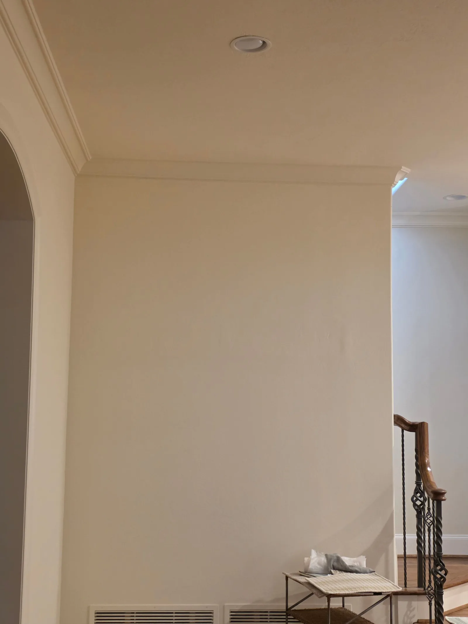 Clean, light beige painted wall with a recessed light in the ceiling and crown molding, next to an arched doorway.
