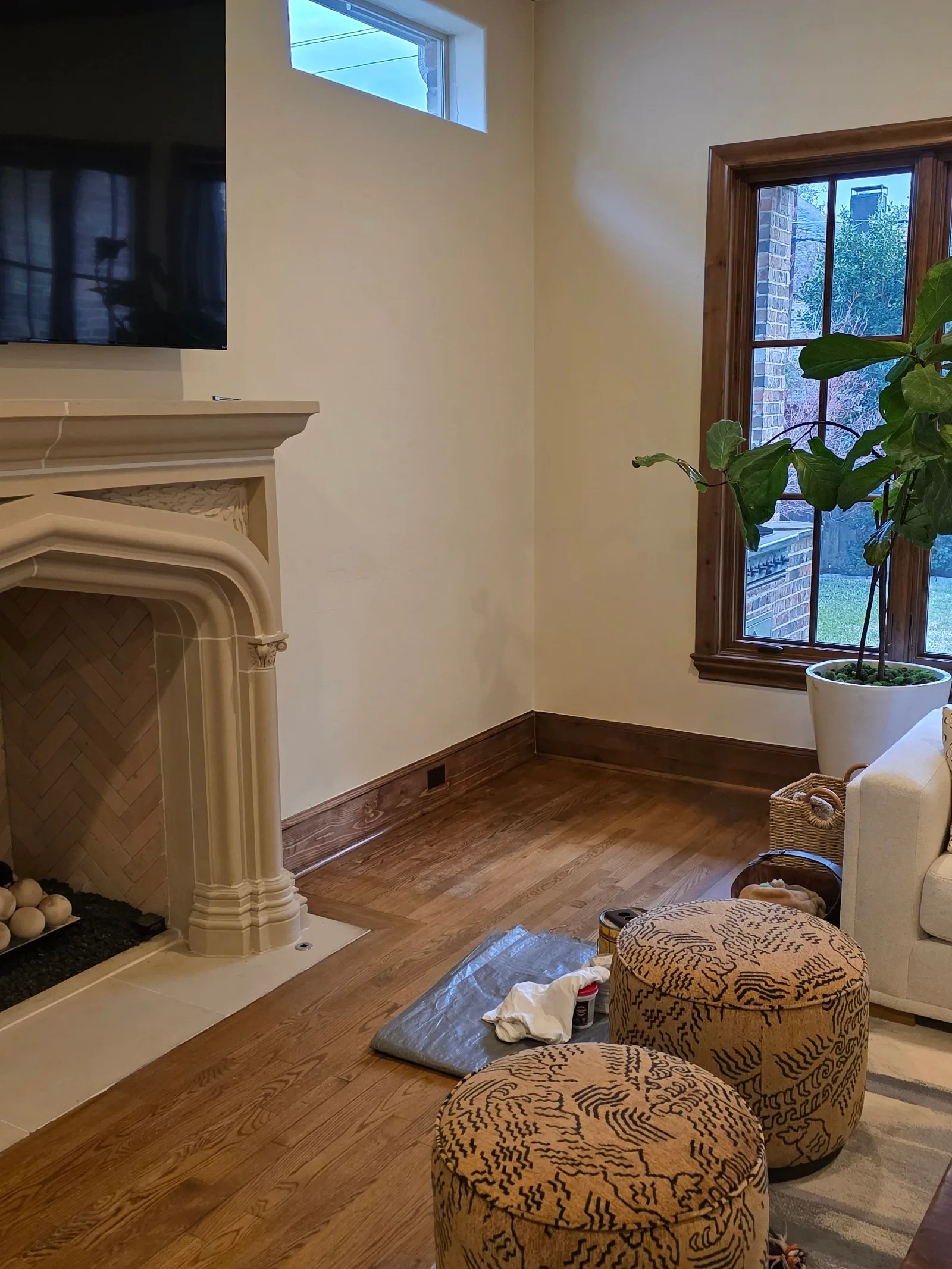 Living room with light beige walls, hardwood floors, a stone fireplace, and a large window with dark wood trim.