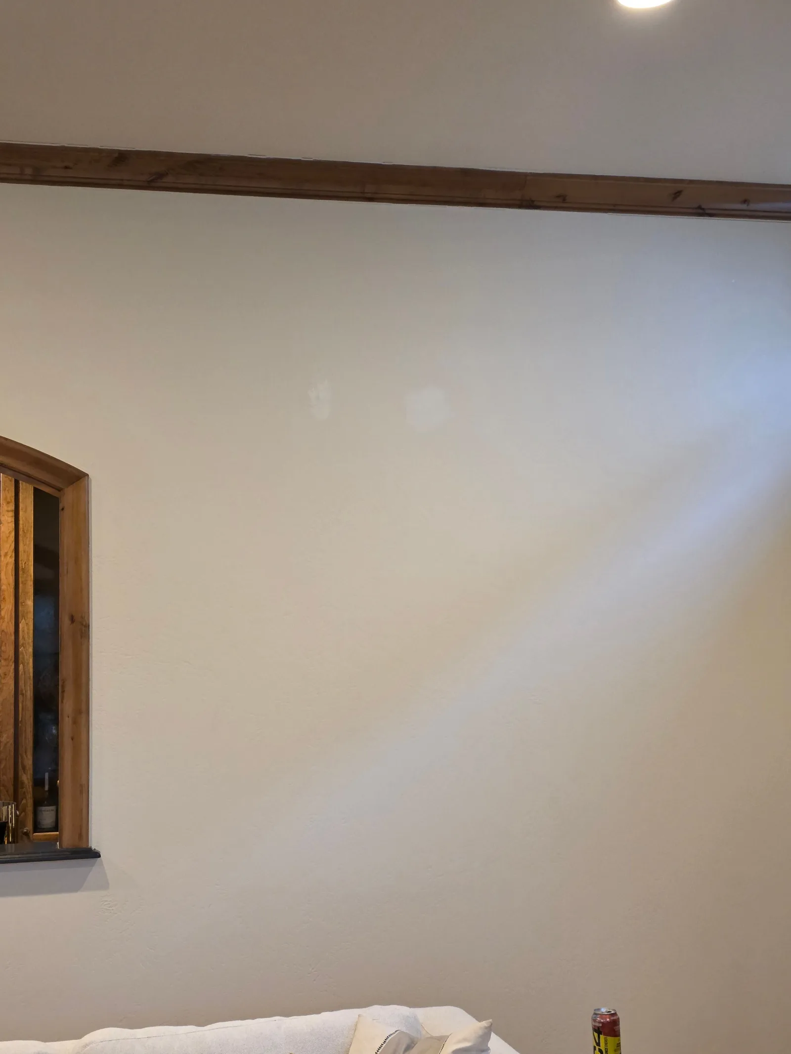 Interior room with white painted walls, a light wood trim beam near the ceiling, and a small arched wood-framed window on the