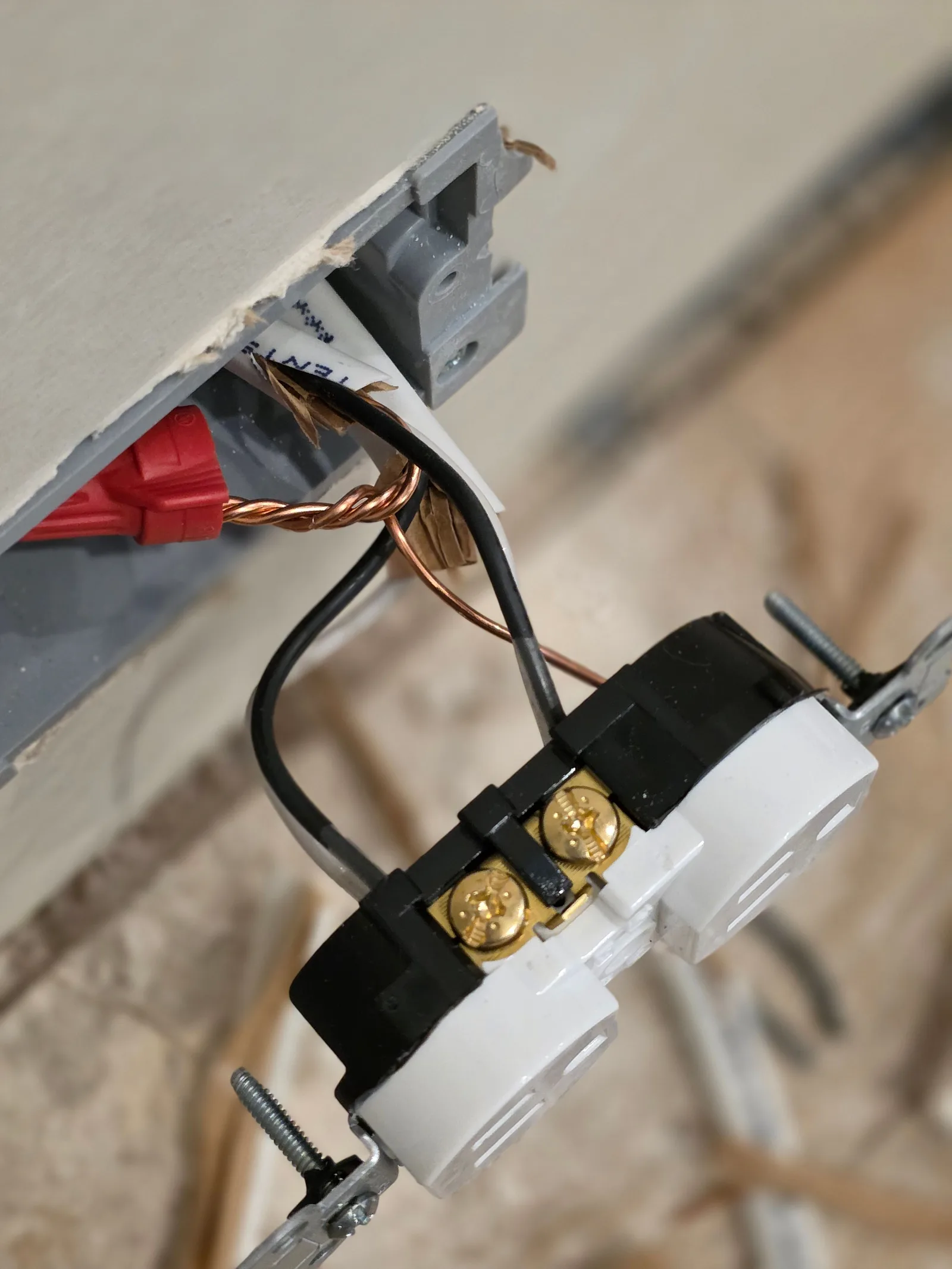 Close-up of a bare electrical outlet with black and copper wires connected to it, partially inserted into a wall cut.