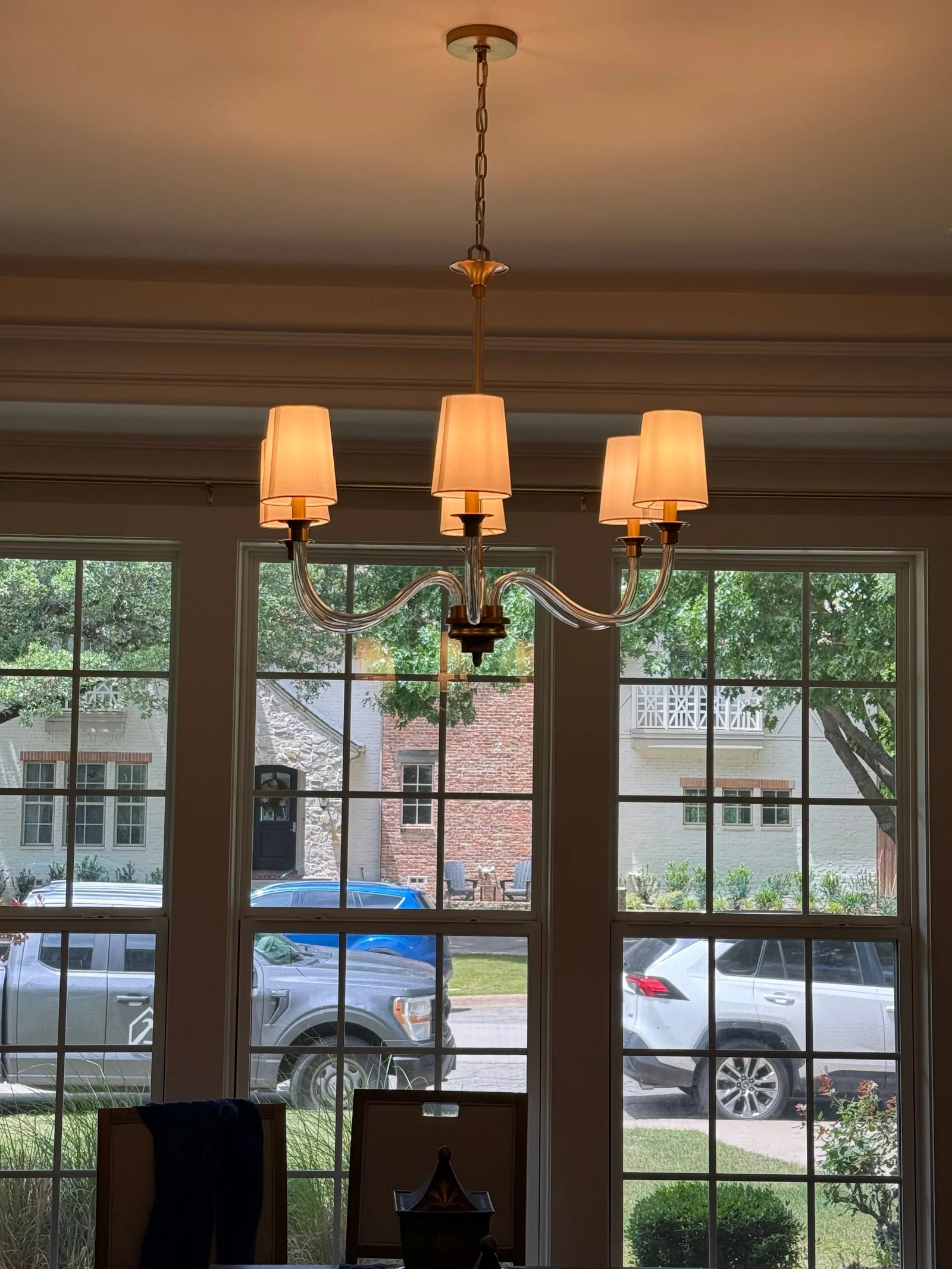 Dining room with a brass and glass chandelier centered above three large windows, revealing neighborhood. The chandelier feat