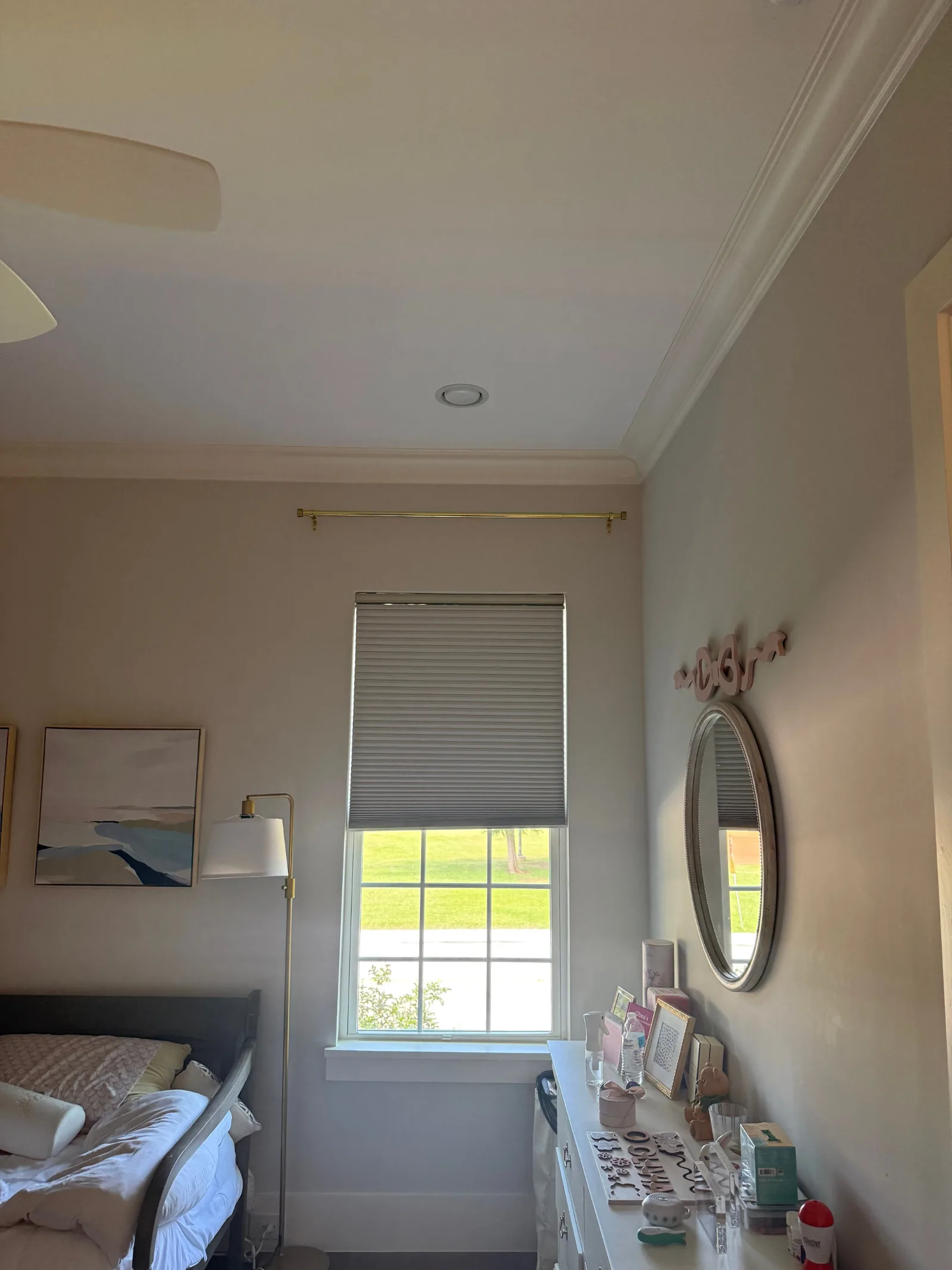 Bedroom with beige walls, white crown molding, large window, golden curtain rod, and ceiling light fixture.