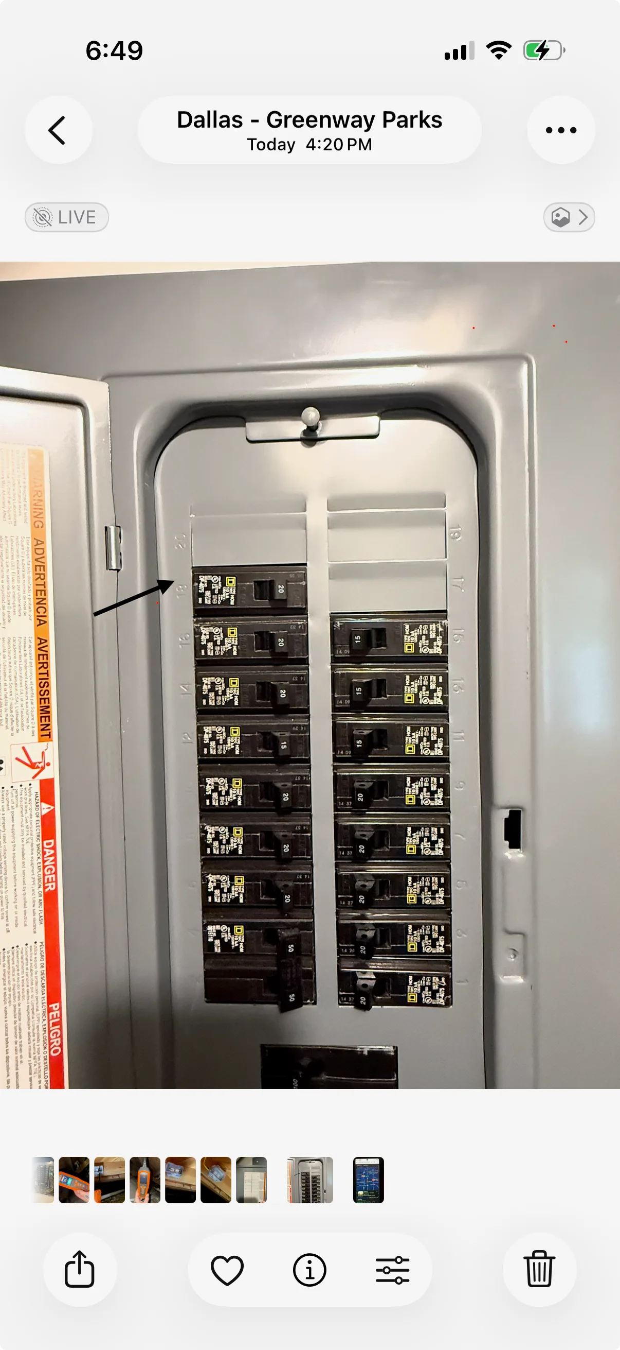 An open electrical panel with a gray metal casing. Multiple black square circuit breakers are visible, each with white number