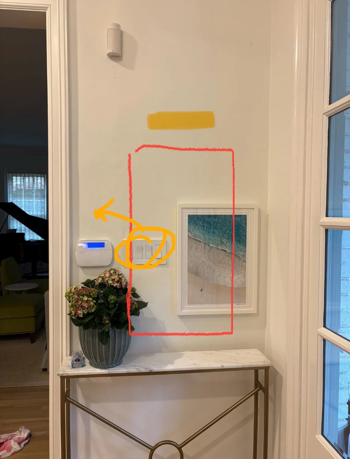 Entryway accent wall with wall-mounted switches, security panel, and framed artwork above a console table.