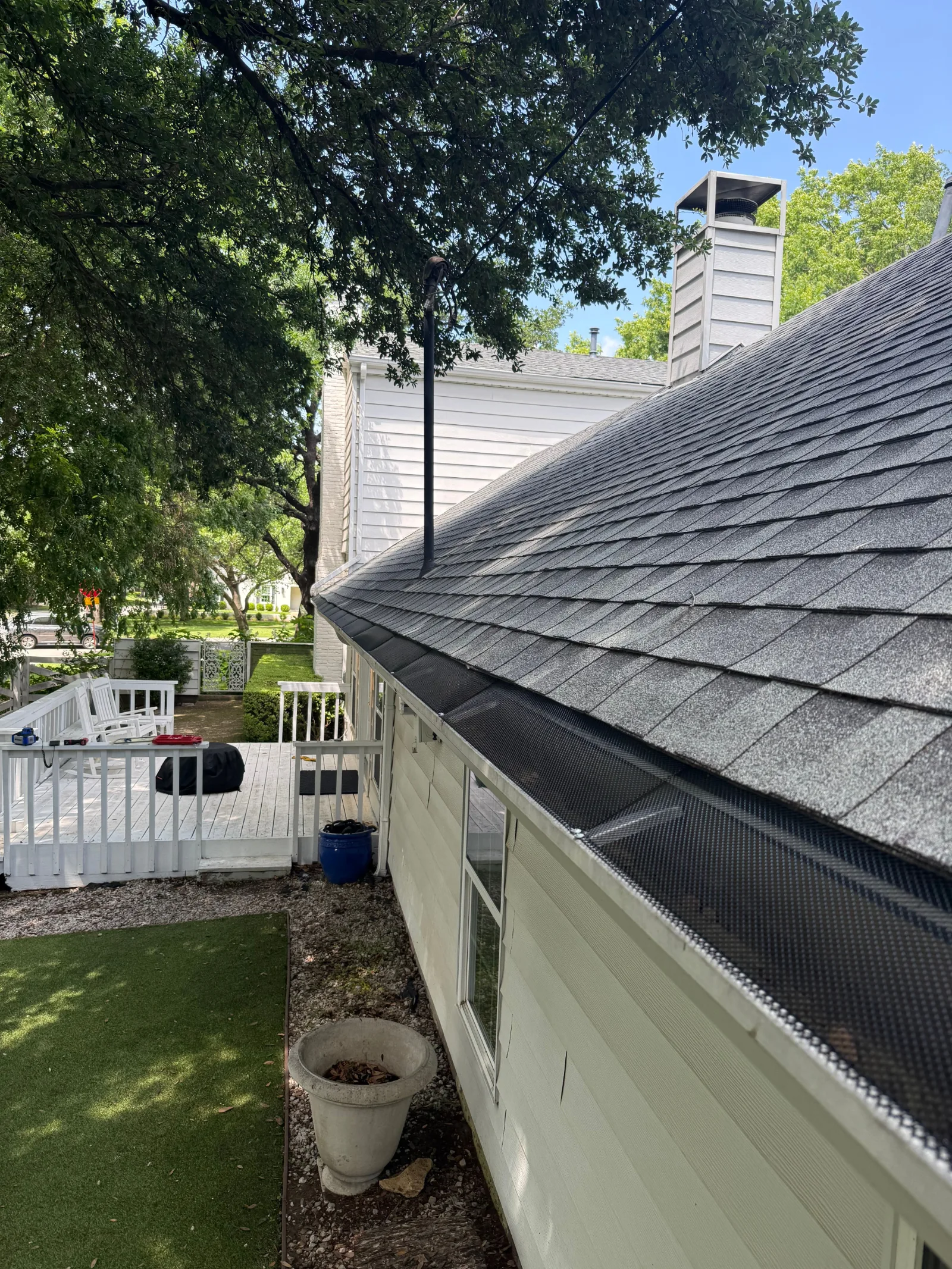 Side view of a house showing a gray asphalt shingle roof with new black gutter guards, white siding, and a white deck.