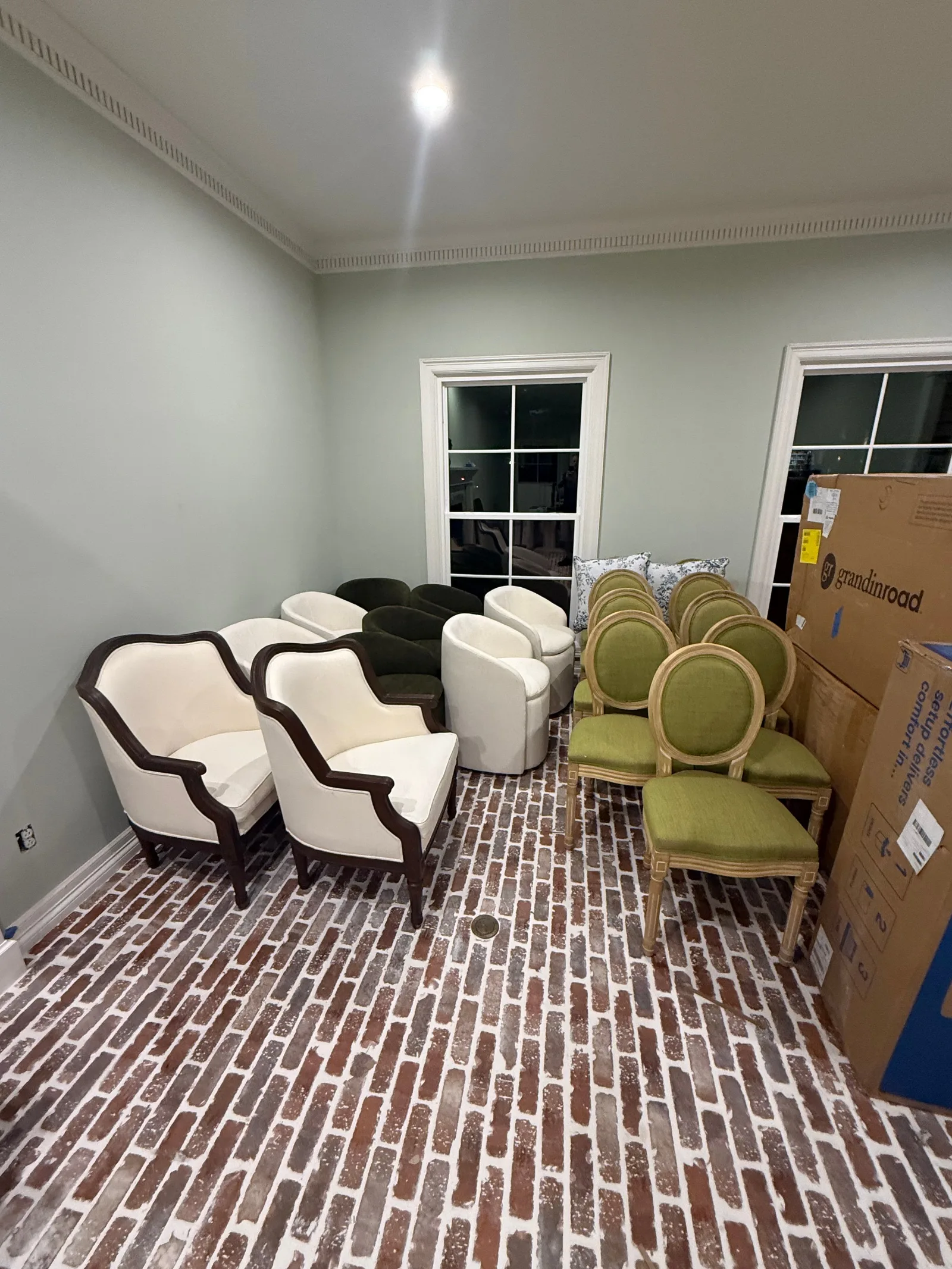 A room with light green walls and brick-patterned flooring. Various chairs in white, green, and dark green are arranged aroun