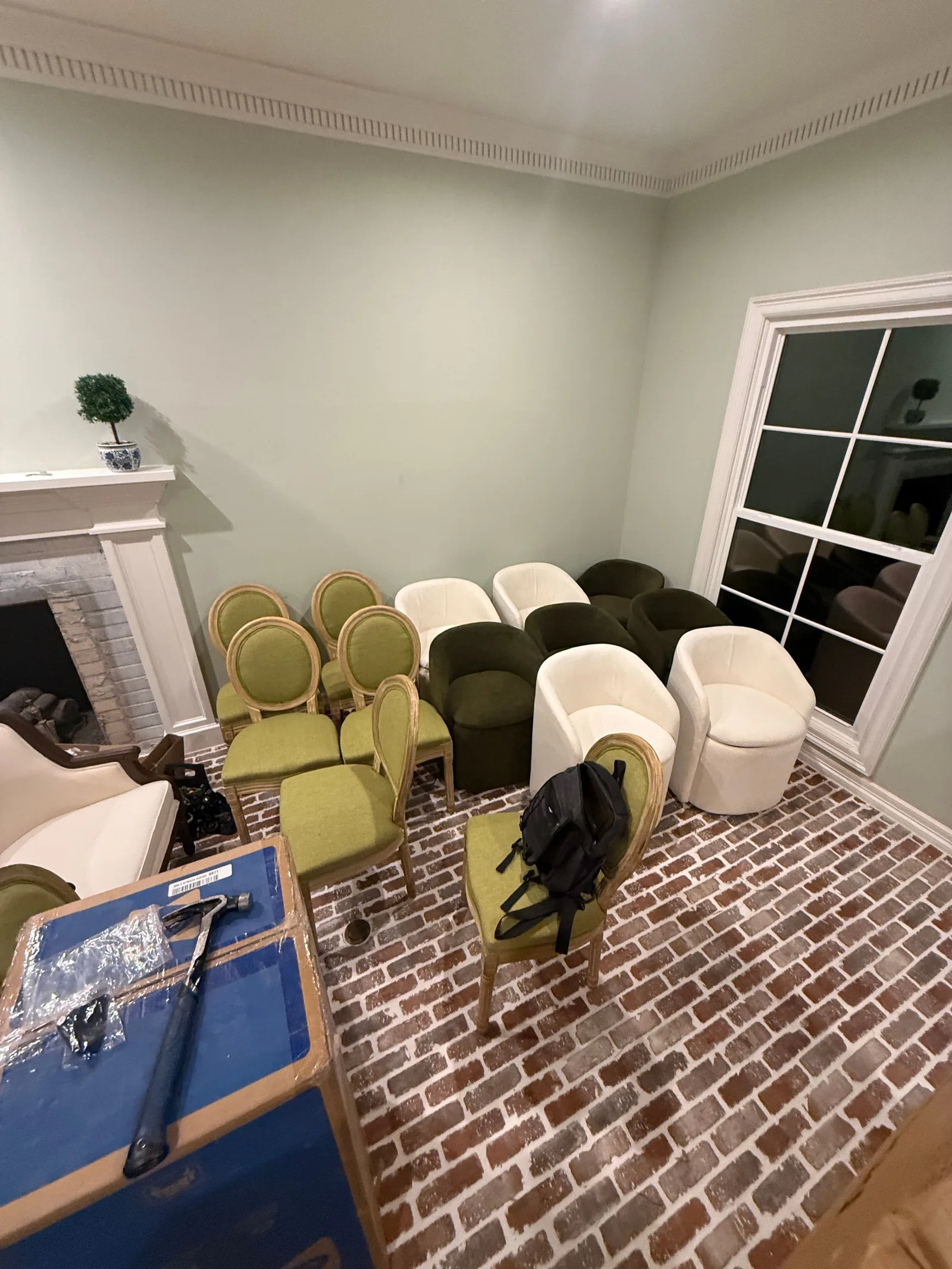 A room with light green walls and a brick-patterned floor. A white fireplace and window frame a collection of green and white