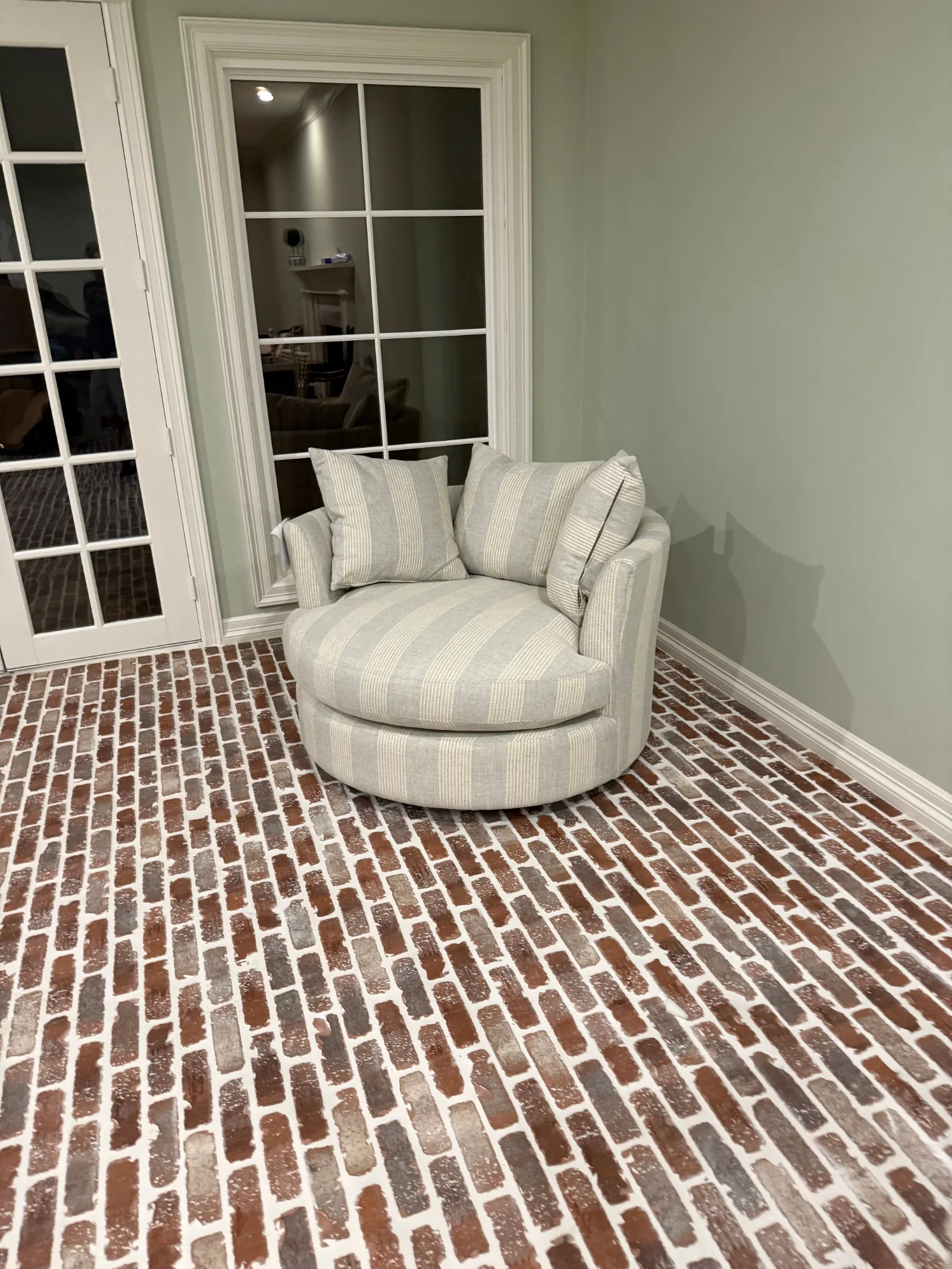 Swivel armchair in grey-striped upholstery with matching pillows on a terracotta brick floor, adjacent to white double French
