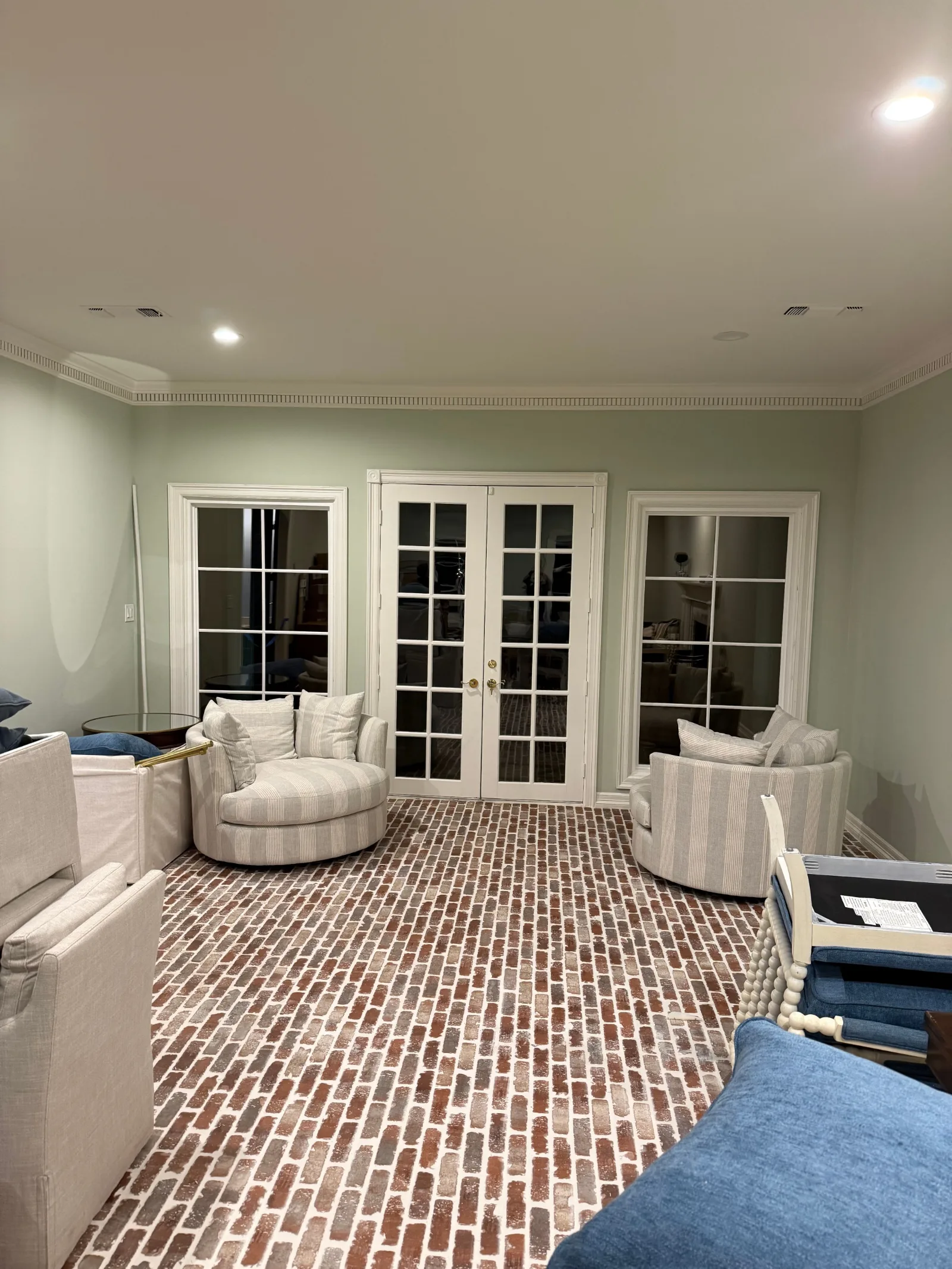 Living room with light green walls, brick flooring, white French doors, and two striped barrel chairs.