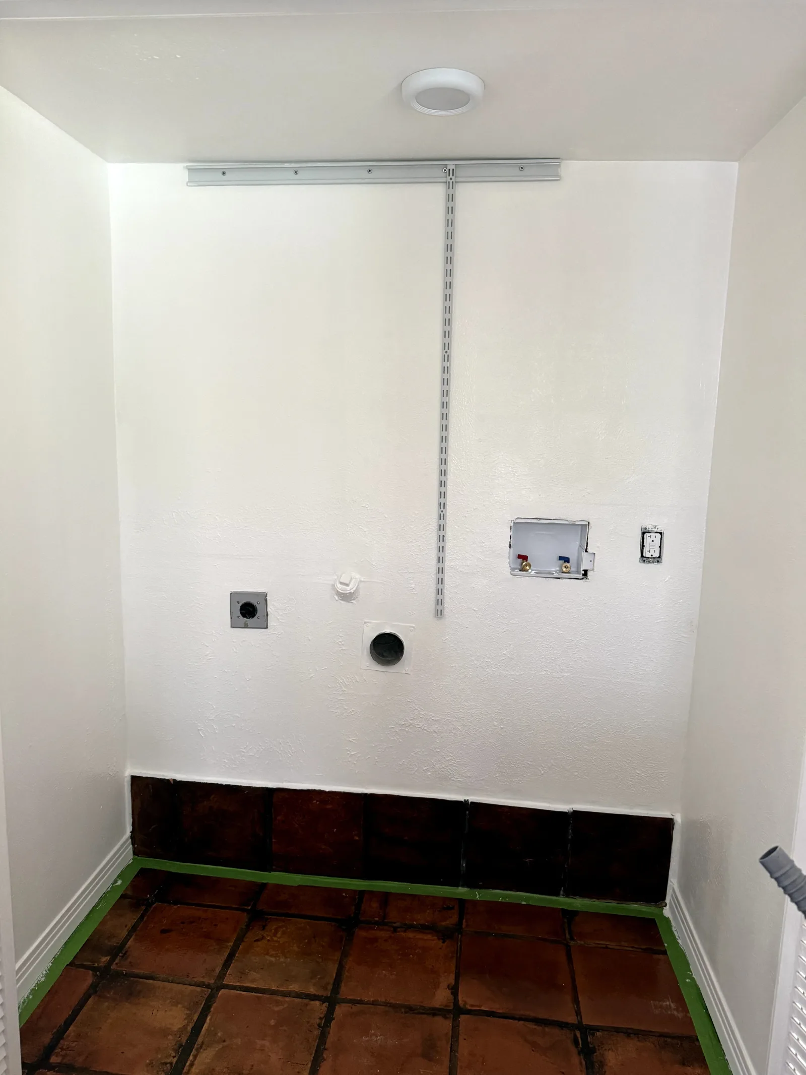 Laundry room with white walls, terracotta tile floor, utility hookups, and a ceiling light.
