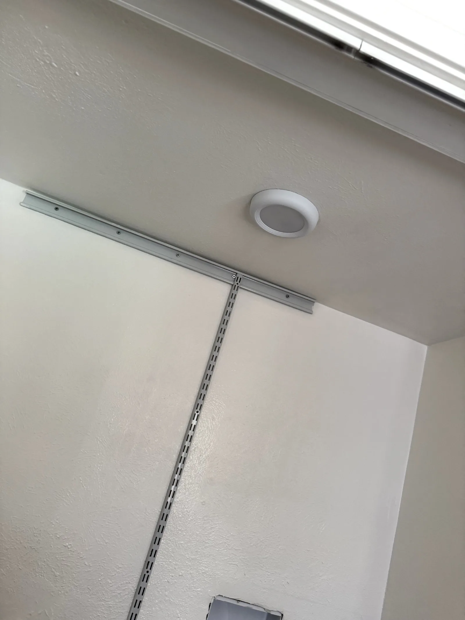 Light gray laundry room wall and ceiling, with mounted white light fixture and gray metal shelving track.