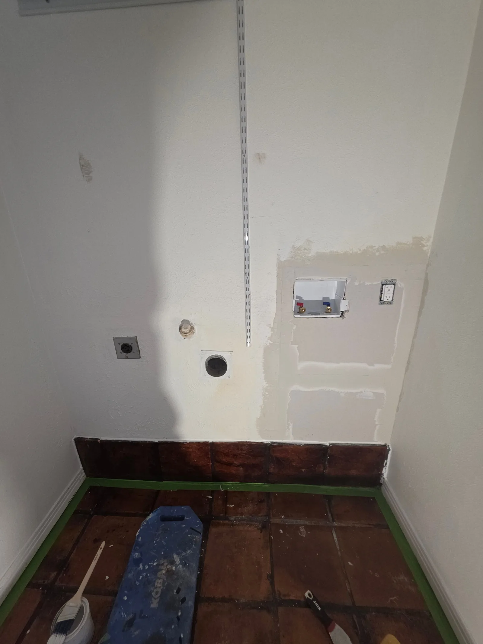 Laundry room with terra cotta tile flooring, freshly spackled walls in preparation for paint, and exposed hookups.