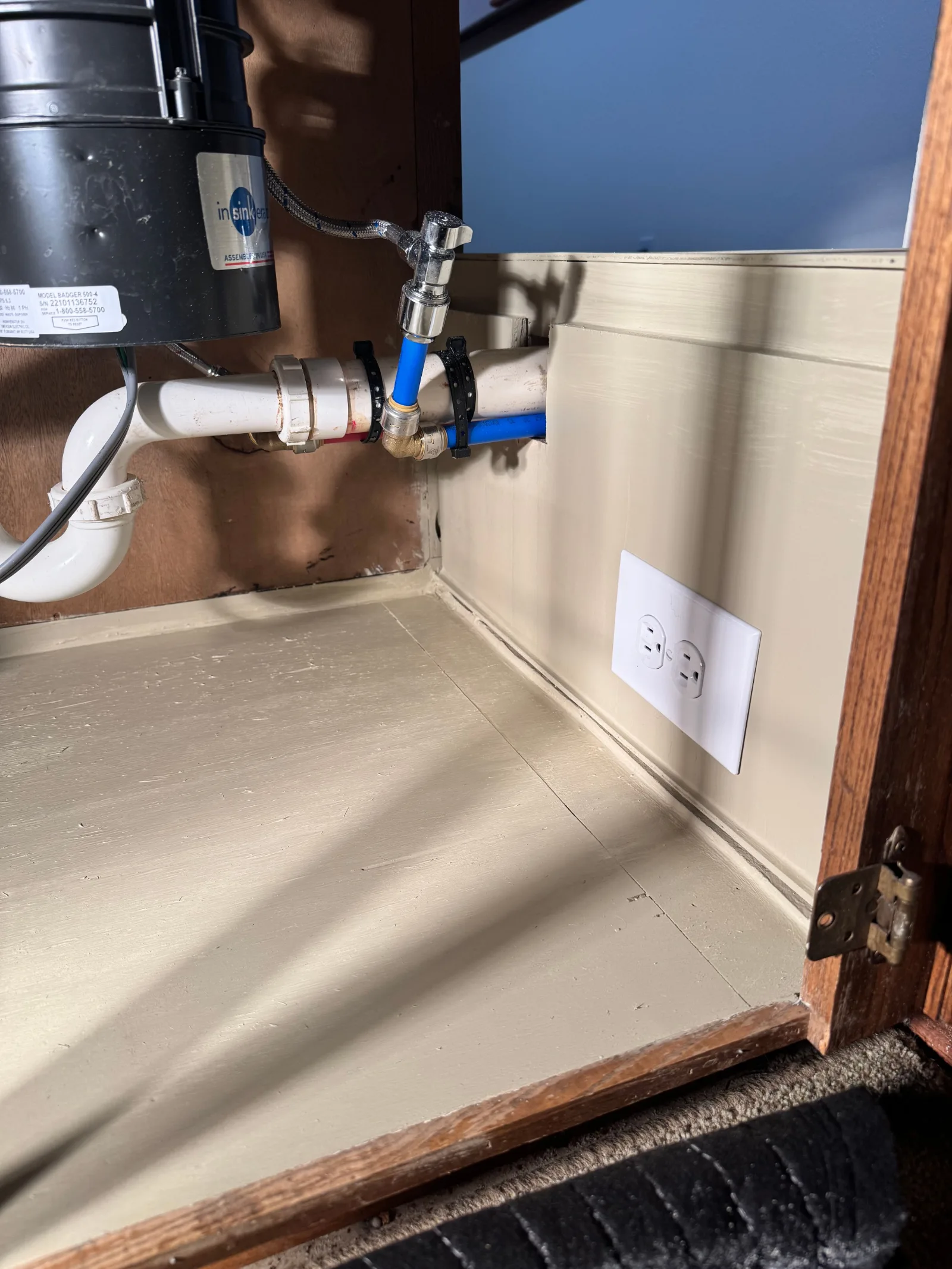 Under-sink cabinet with a garbage disposal, white P-trap, and blue PEX lines connected to a chrome shut-off valve. The cabine