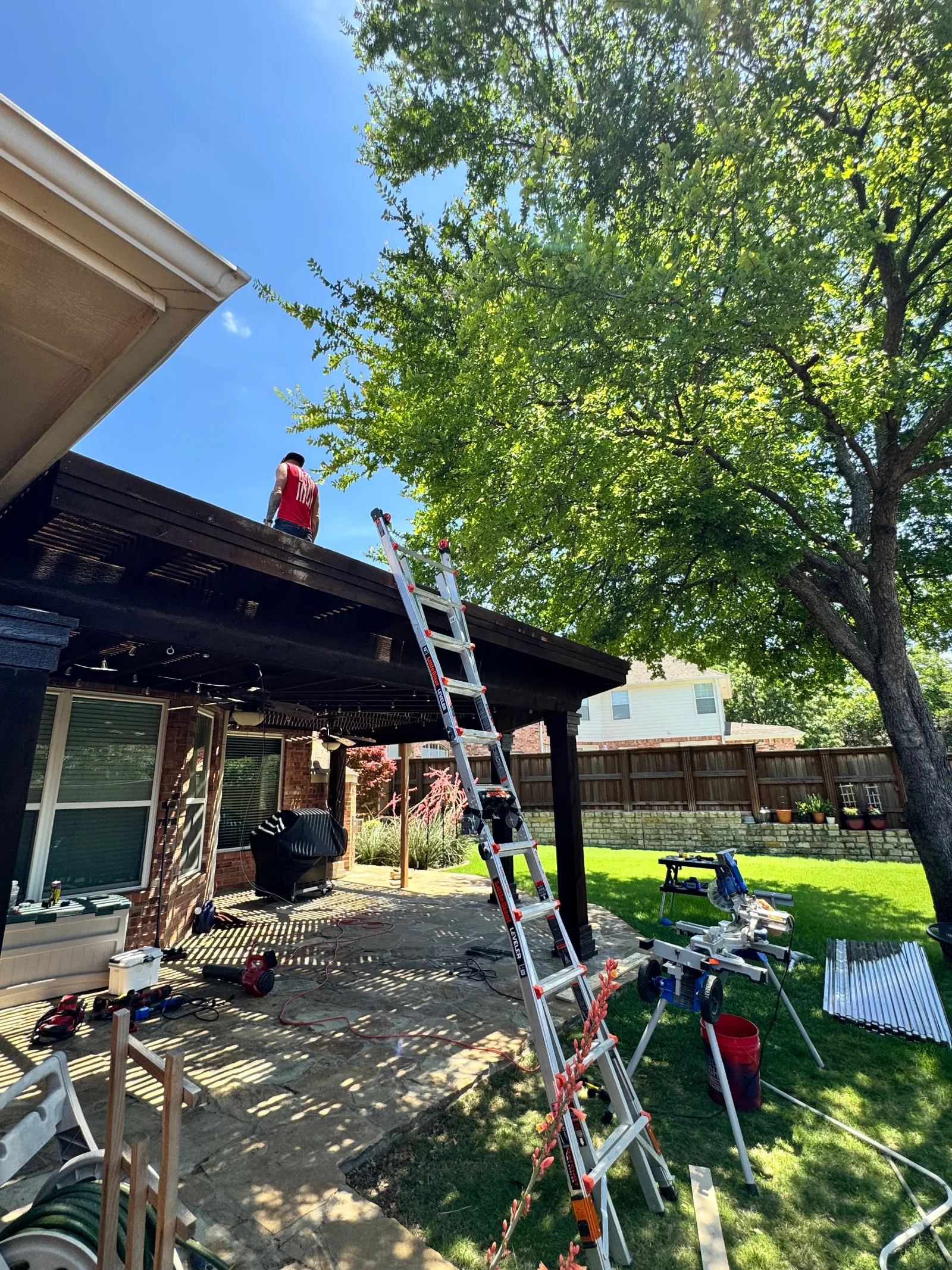 A Creative Constructors tech standing on top of a dark wood pergola over a flagstone patio.