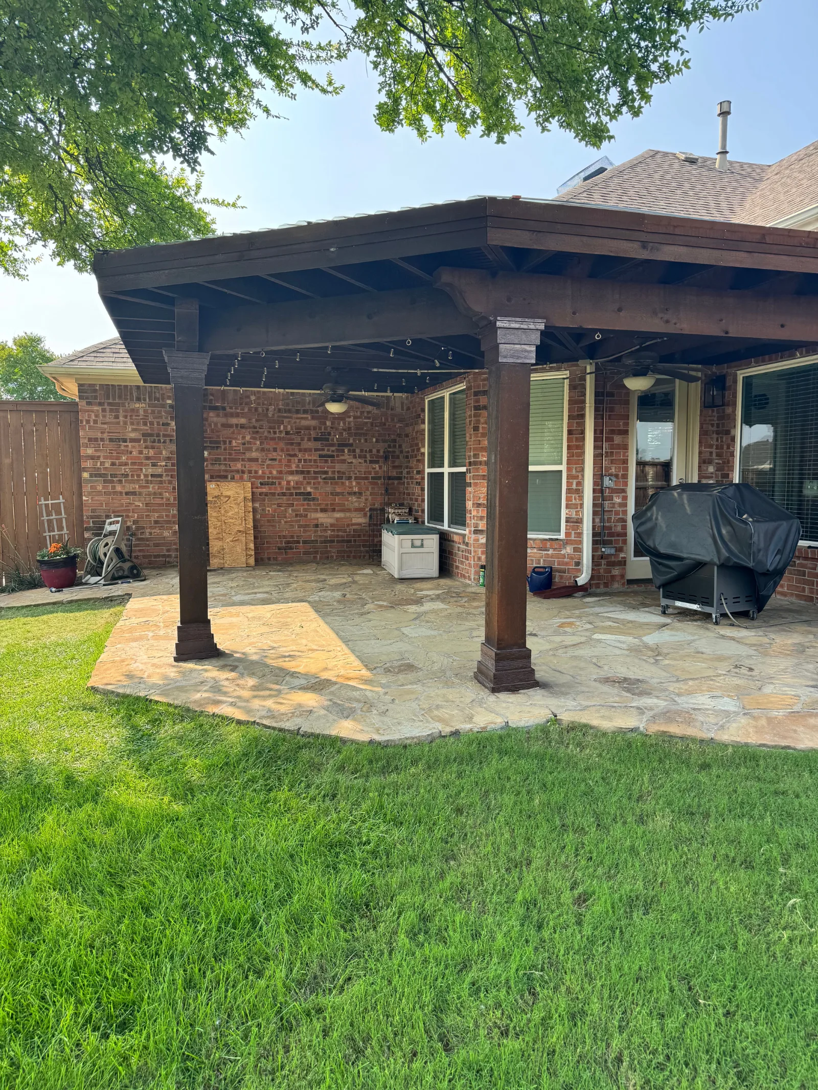 Backyard patio with a dark wood pergola, clear polycarbonate roof, and irregular flagstone paving.