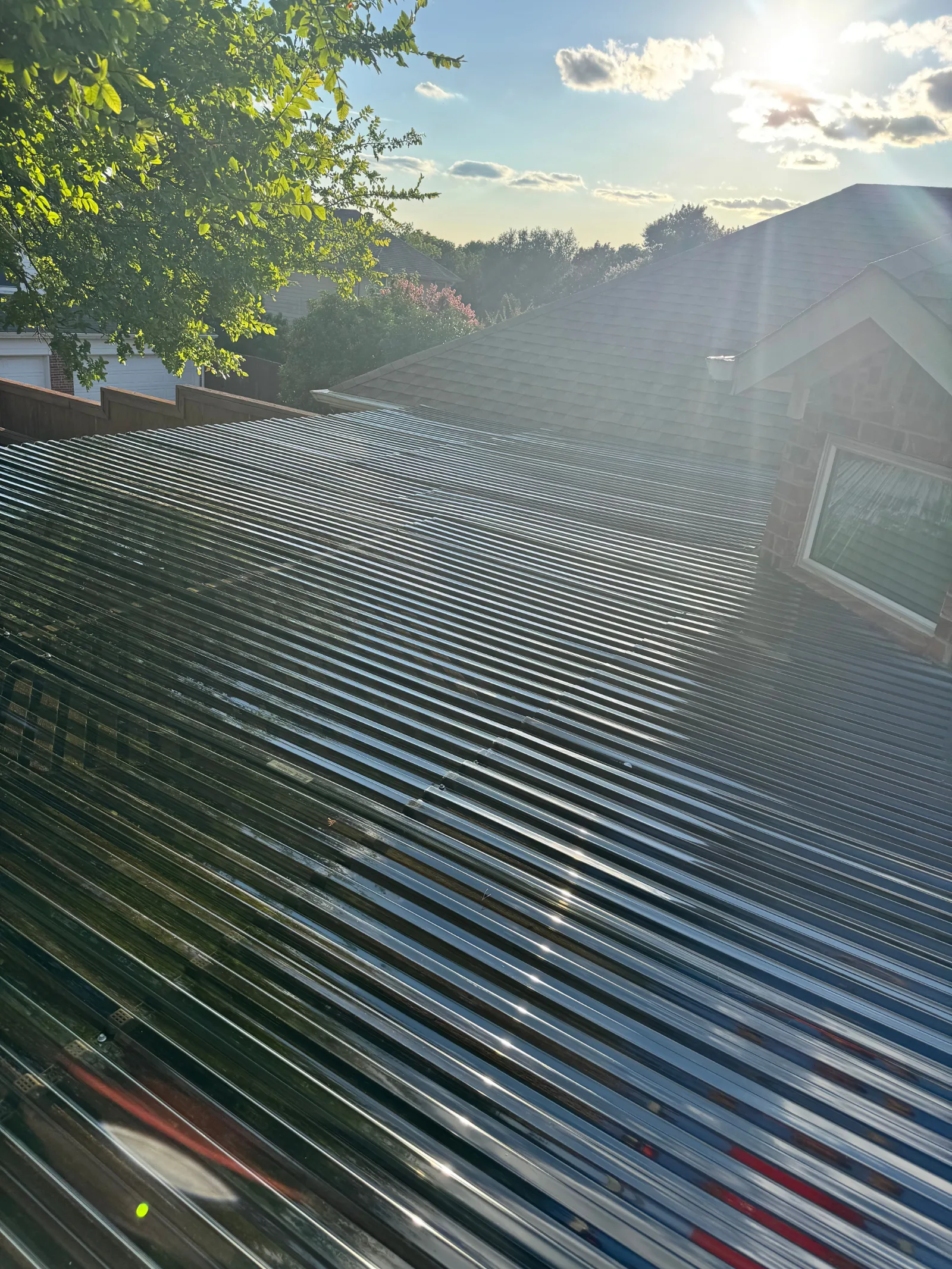 Top-down view of a newly installed corrugated clear polycarbonate roof with direct sunlight and reflections.