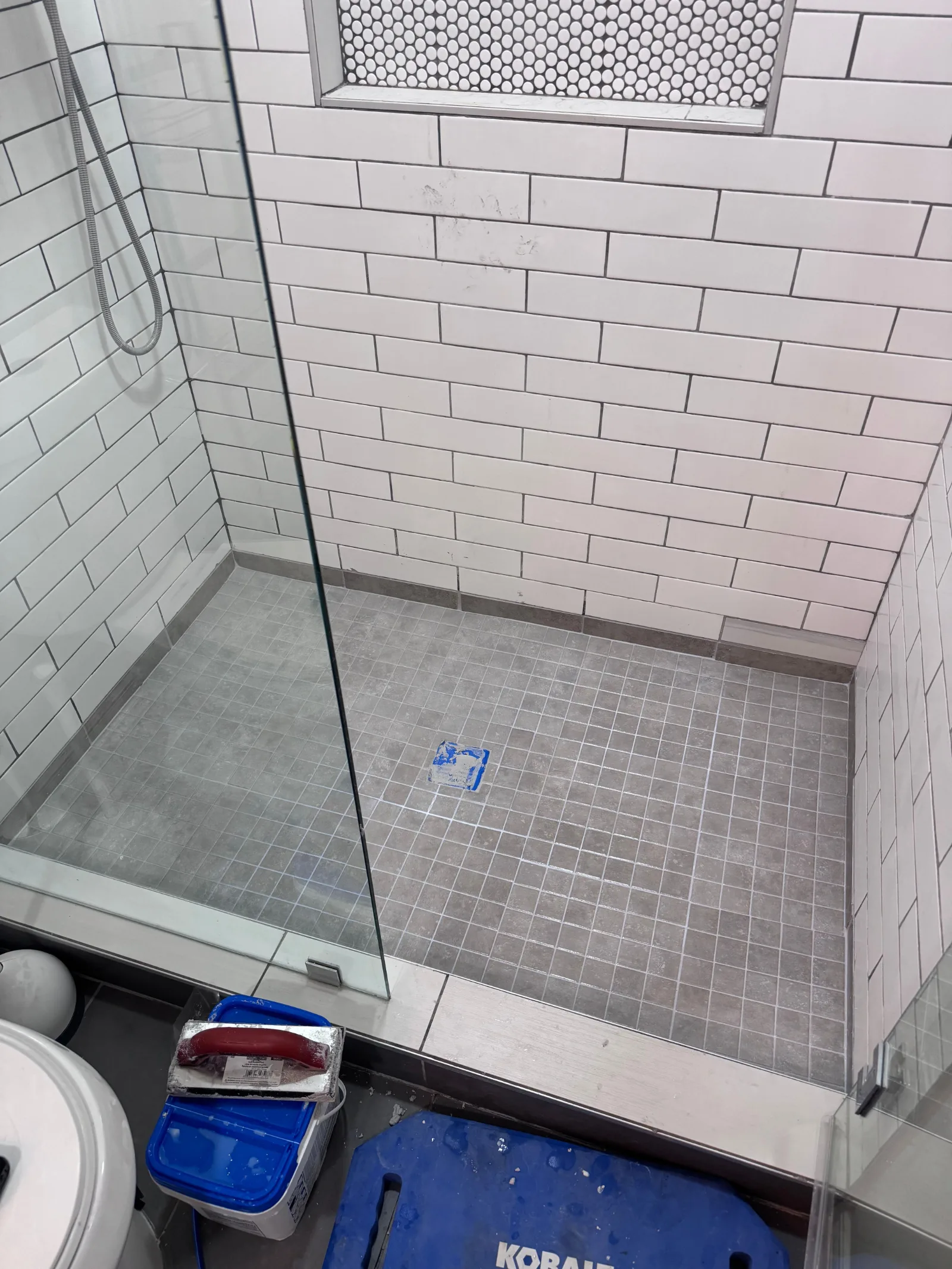 Newly tiled shower with white subway tiles on walls, gray square tiles on the floor, and a penny tile niche.