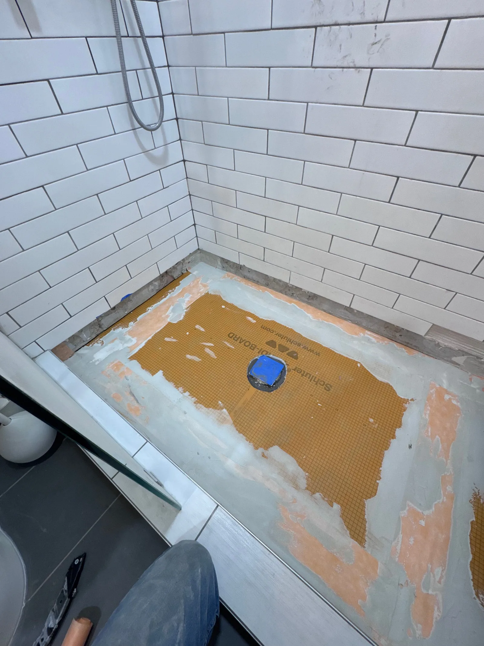 Shower stall with white subway tile walls, a Schluter-DITRA shower pan base, and a blue drain cover awaiting new tile.