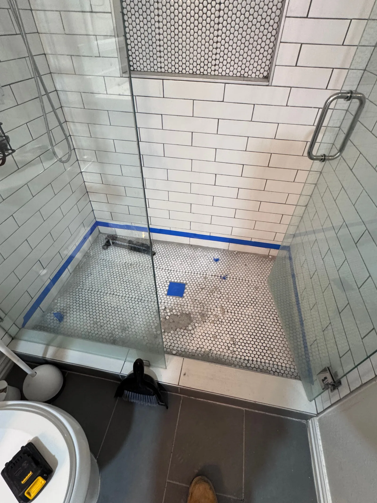Bathroom shower with white subway tile walls, white penny tile floor, glass shower door, and blue tape marking areas for repa
