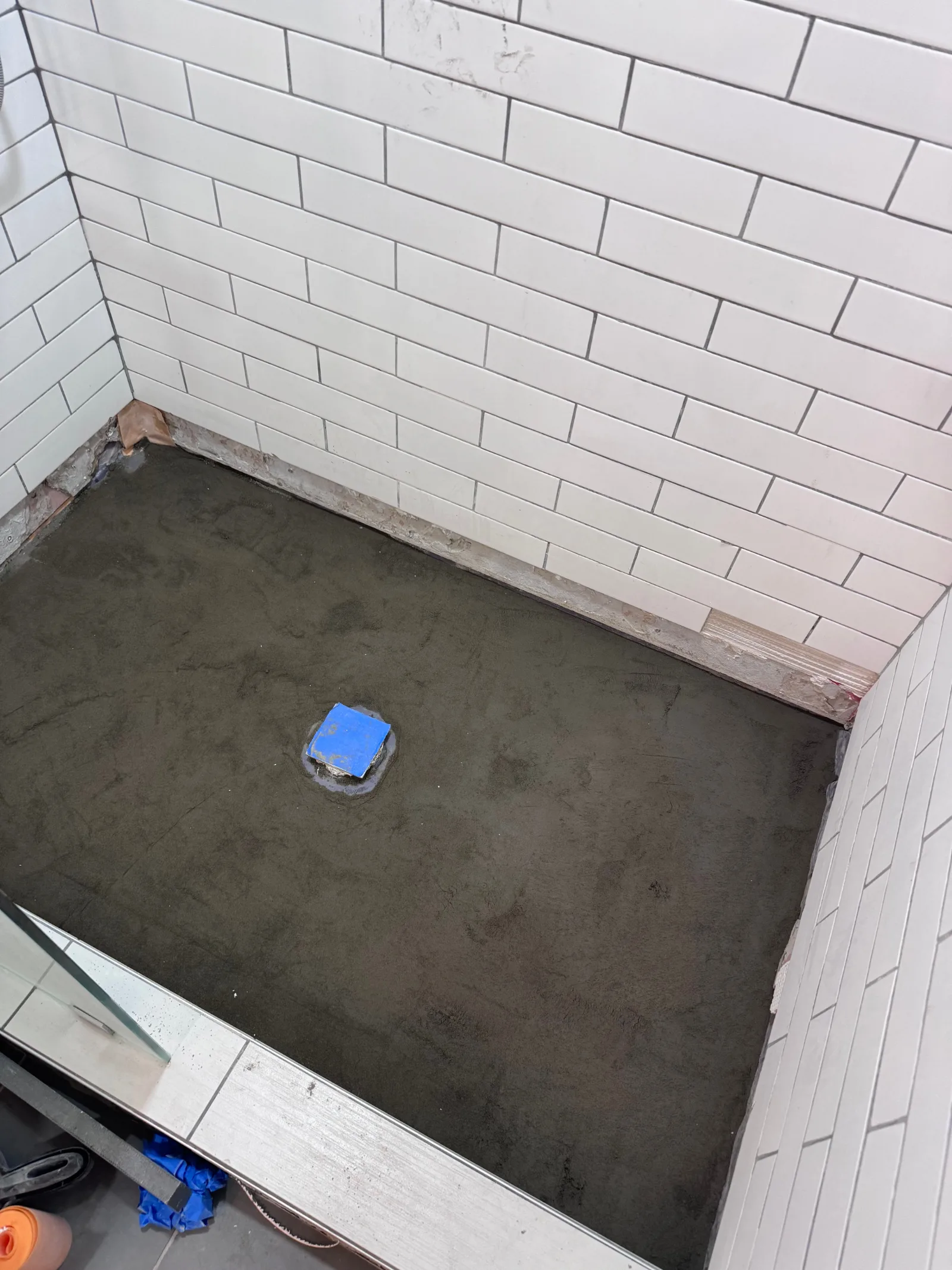 Shower pan mud bed, a blue taped drain, and white subway tile walls.