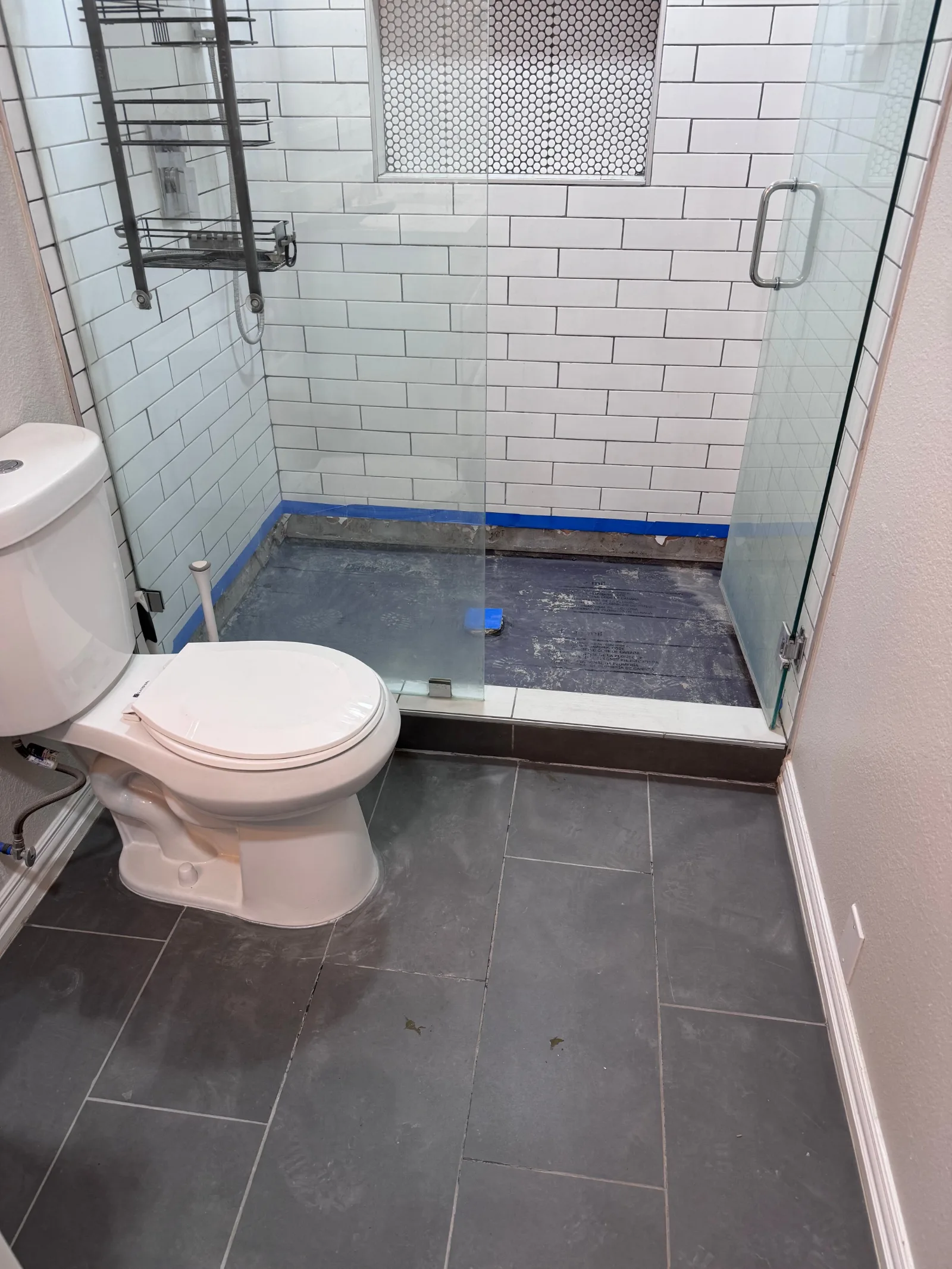 Bathroom shower with white subway tile walls, a niche with hexagon mosaic tile, and a glass door. The shower pan is exposed.