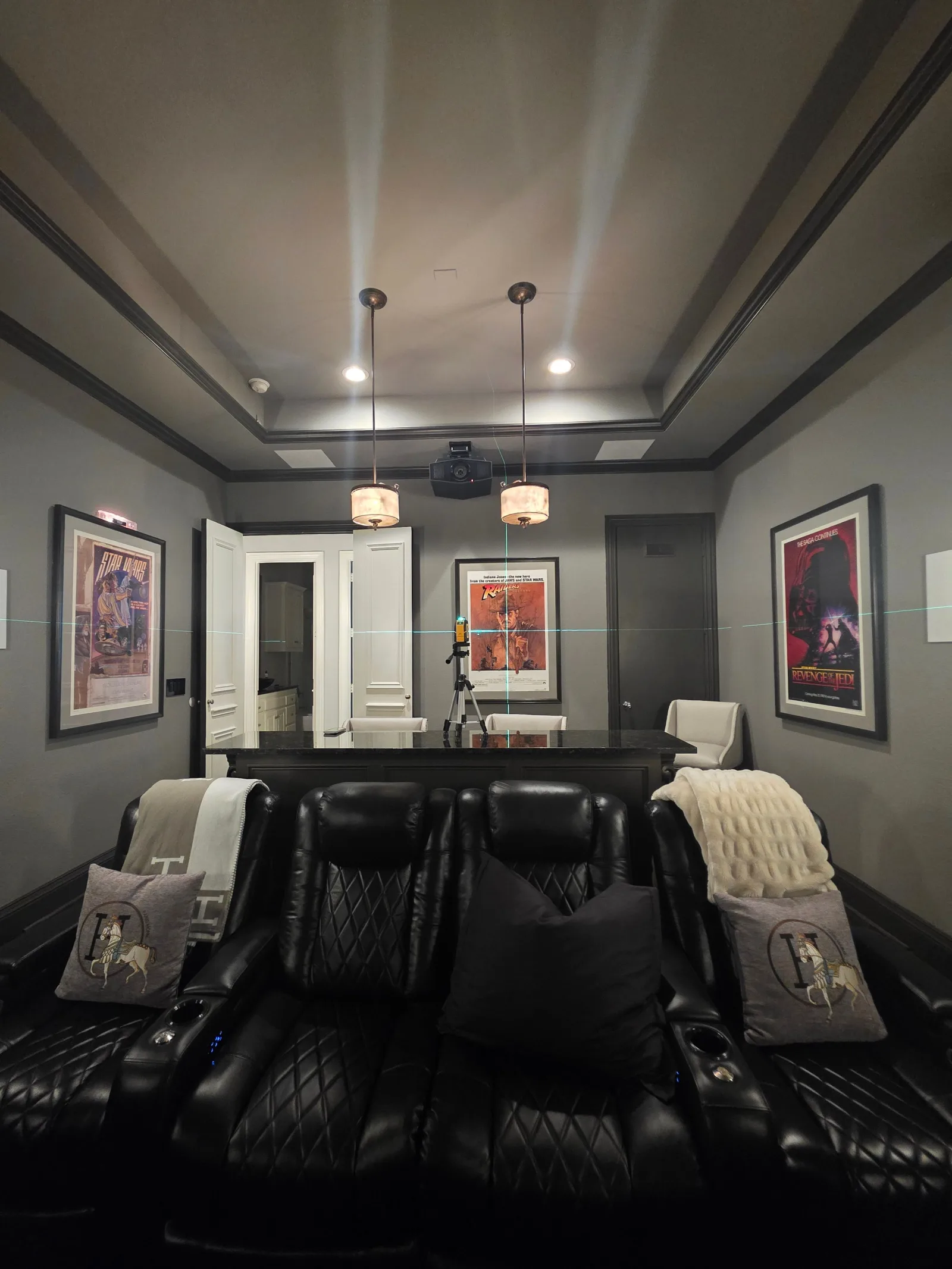 Home theater with black leather recliners, dark gray walls, white double doors, and framed movie posters.