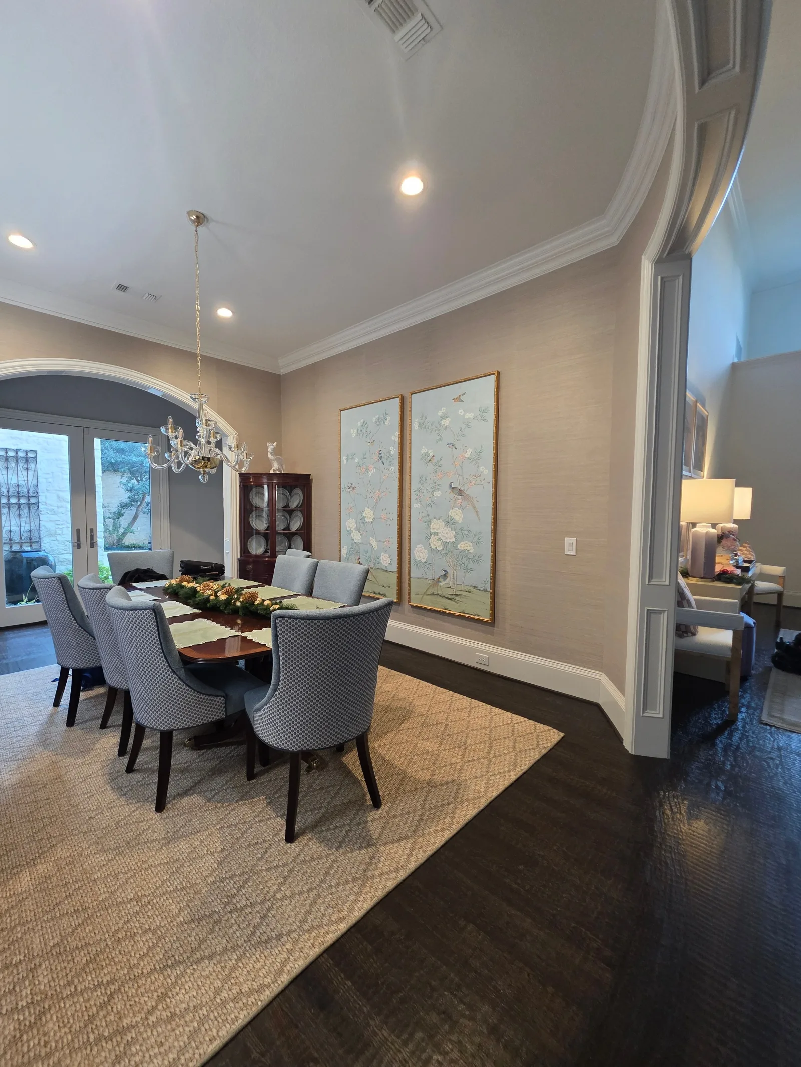 Dining room with a long dark wooden table surrounded by eight blue upholstered chairs, set on a natural fiber rug.