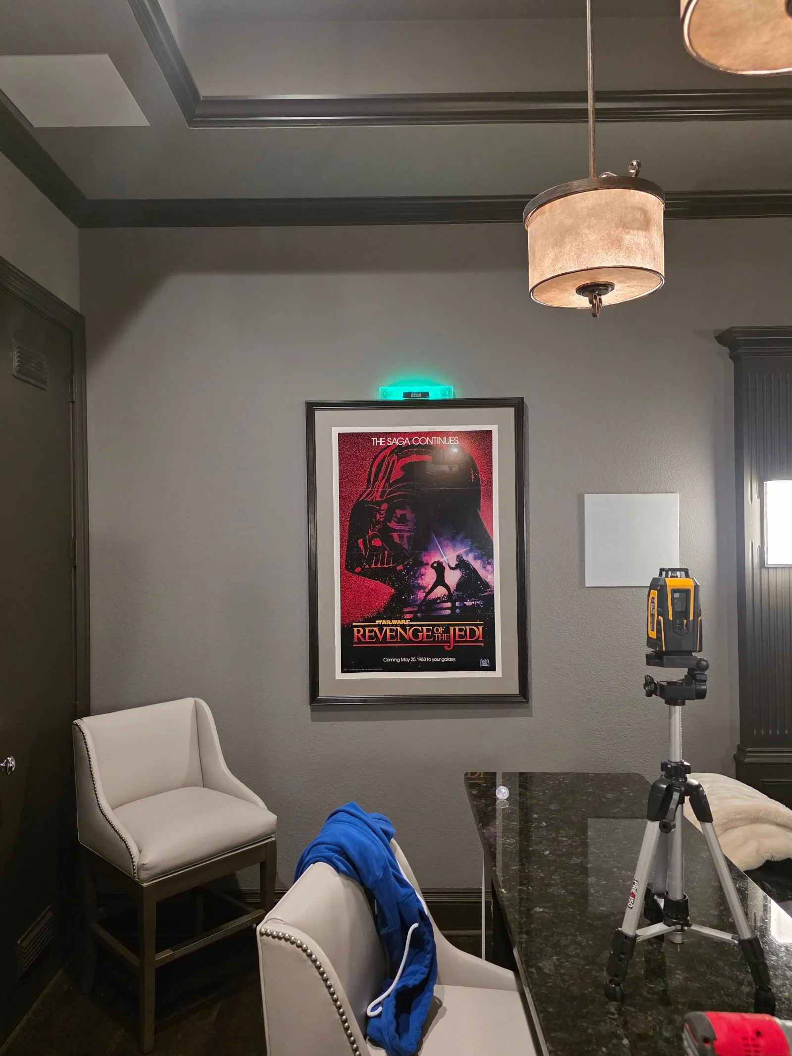 Interior room with a Star Wars poster on a grey wall, two upholstered chairs, a dark granite counter, and a laser level on a