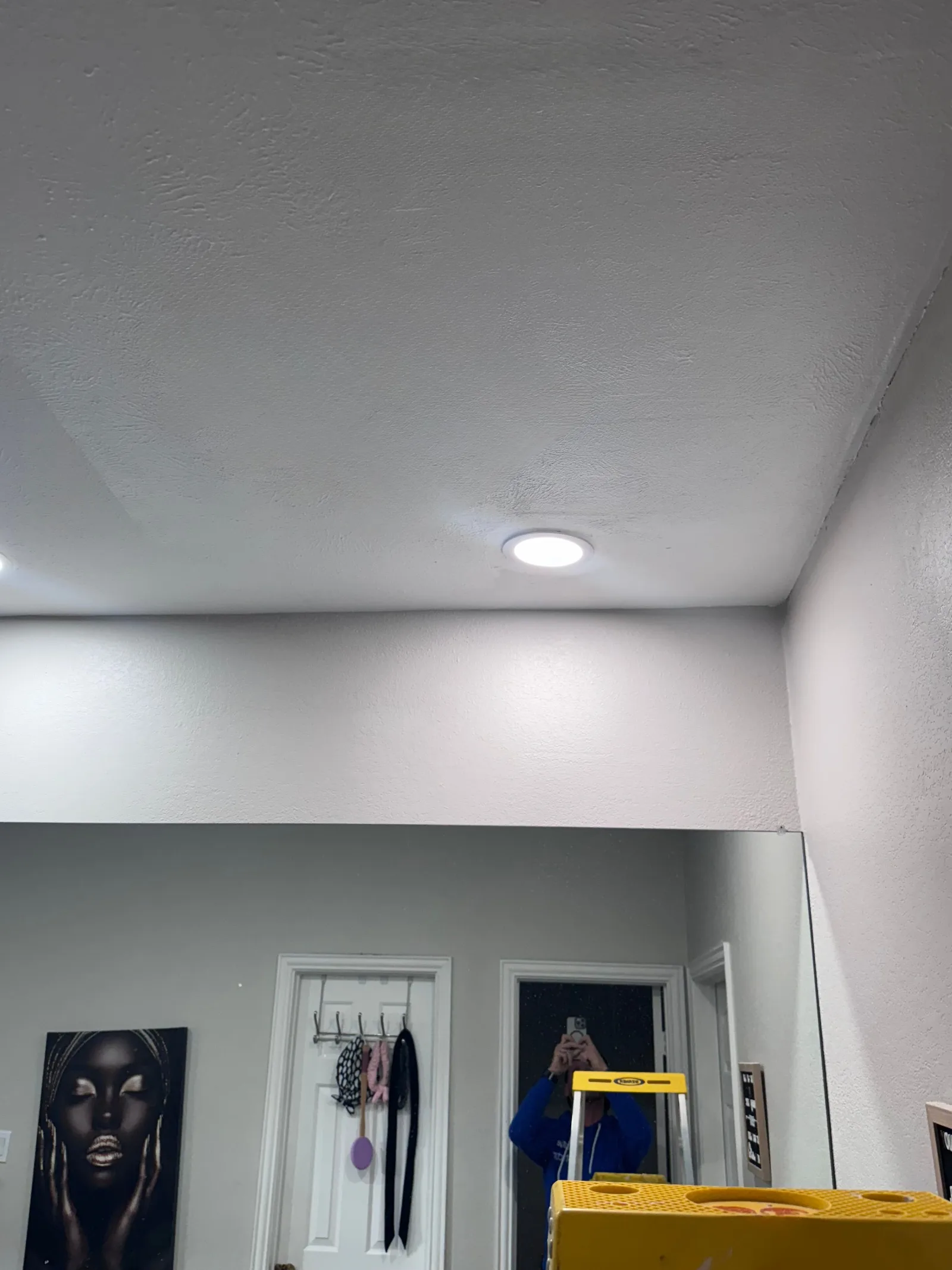 Smooth white ceiling with visible texture features, light gray walls, one recessed light fixture, and a large mirror.