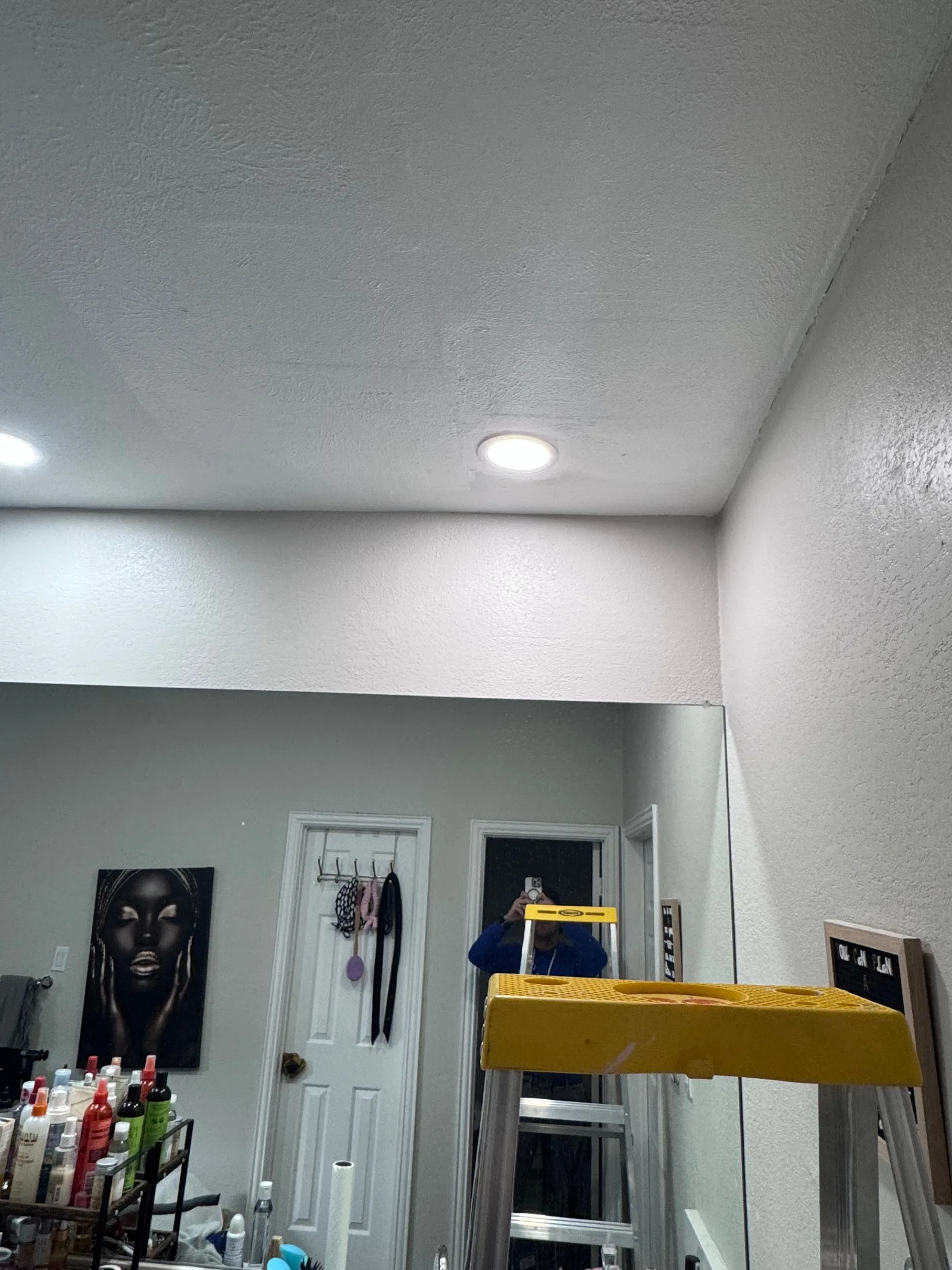 Bathroom with a textured white ceiling, white textured walls, recessed lighting, and a large mirror. A ladder and various hai