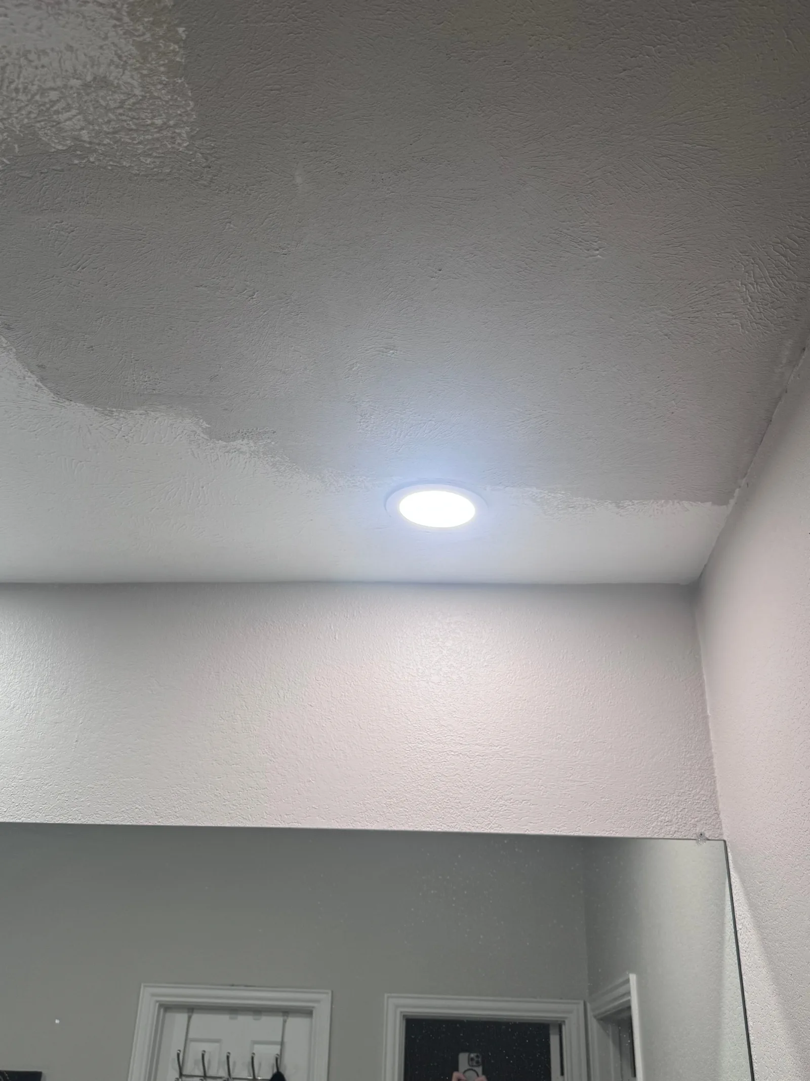A bathroom ceiling and walls with a large mirror. The white textured ceiling shows water damage with visible staining around